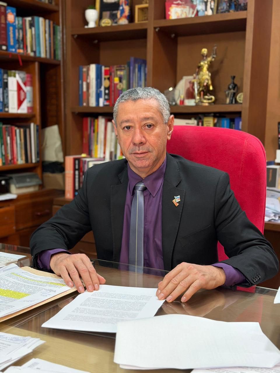 Ednaldo Vidal sentado à mesa de trabalho, diante de uma estante de livros